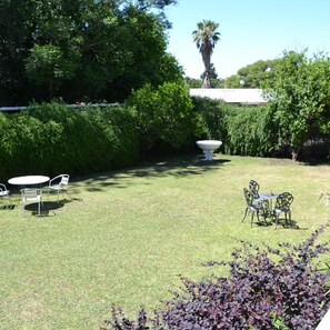 Ein gepflegter Garten mit Rasen, zwei Tischen mit Stühlen und einem großen Zierkübel.