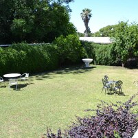 Un jardín bien cuidado con césped, dos mesas con sillas y una maceta decorativa grande.