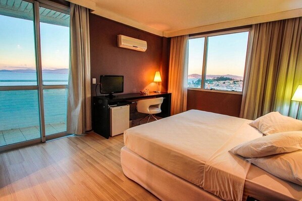 A hotel room with a bed, desk, chair, and a view of the sea. - Encantos Golden Hotel (Sao Jose)