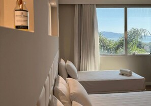 Een hotelkamer met een bed, een raam met uitzicht op zee en een fles wijn aan de wand.