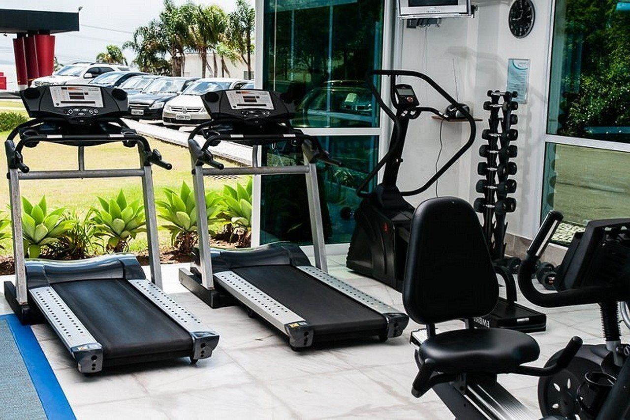 Uma academia com esteiras, uma elíptica e um banco de musculação.