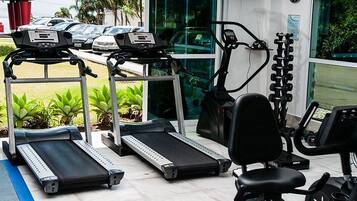 Uma academia com esteiras, uma elíptica e um banco de musculação.