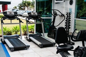 Uma academia com esteiras, uma elíptica e um banco de musculação.