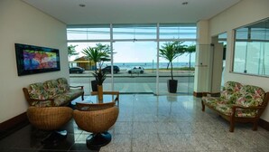 Un vestíbulo con vista a la playa, dos sillas de mimbre, una mesa de centro y un cuadro en la pared.