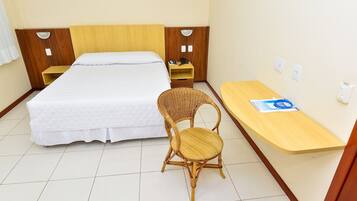 Quarto de hotel com cama, cadeira, escrivaninha e mesa de cabeceira.