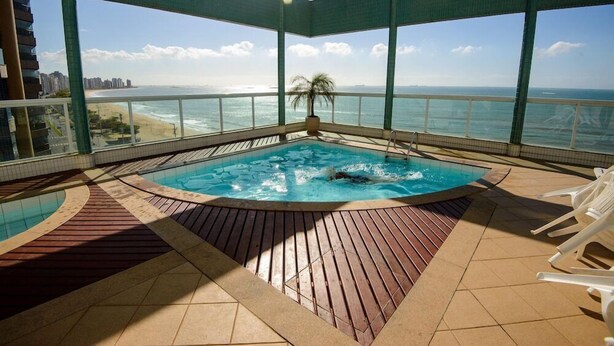 Un área de piscina en la azotea con un jacuzzi, terraza de madera y vista a la playa y al océano.