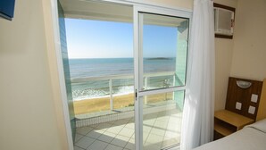 Habitación de hotel con puerta corrediza de vidrio que da a un balcón con vista a la playa.