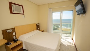 Habitación de hotel con cama, escritorio, teléfono, televisión y vista a la playa.