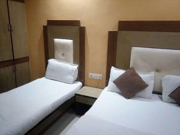 Two single beds with headboards and pillows, a bedside table with a lamp, and a wardrobe complete this cozy space.