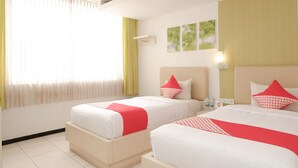 A hotel room with two beds, a window with curtains, a wall-mounted light, and a small table with bottles. - Ebizz Hotel Jember (Jember)