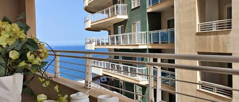 A balcony with a table set for tea, overlooking a building with multiple balconies and a view of the sea.