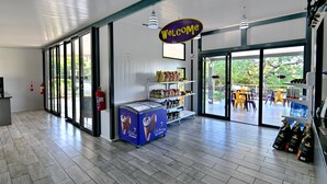 A spacious indoor area with a 'Welcome' sign, a large ice cream freezer, shelves stocked with snacks, and a view through glass doors to an outdoor seating area.