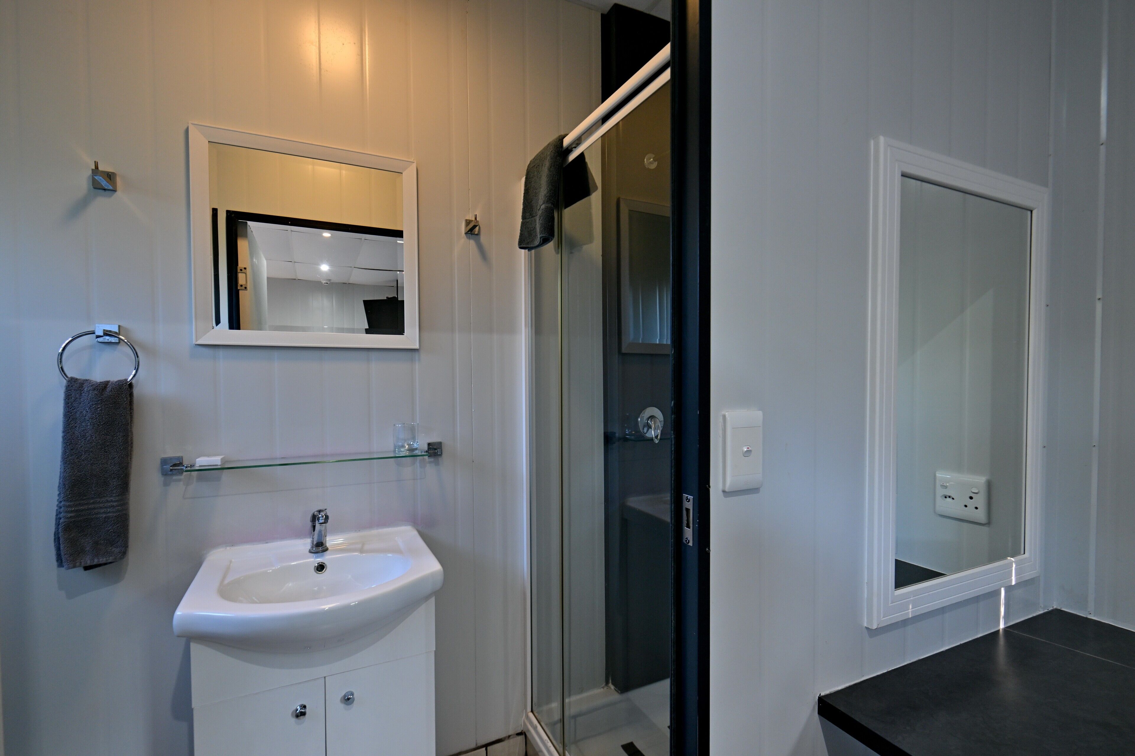 Un baño con lavamanos blanco, un espejo, cabina de ducha de vidrio y un perchero para toallas.