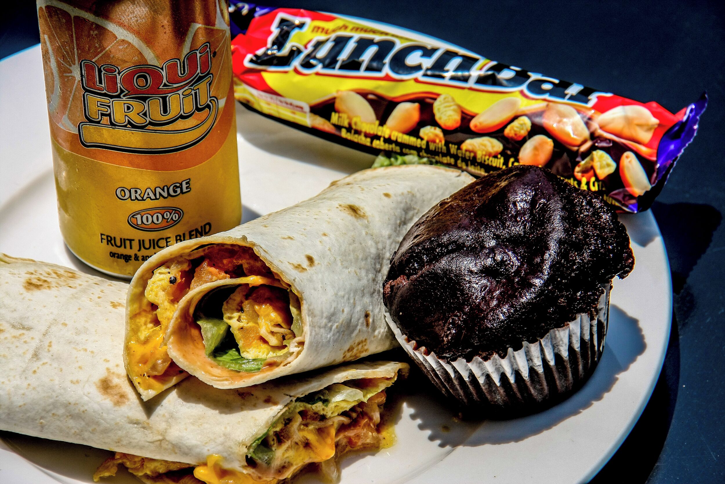 En tallrik med en burrito, en chokladmuffin och en dryck märkt med texten ”LIQUI FRUIT Orange 100 % fruktjuice”.