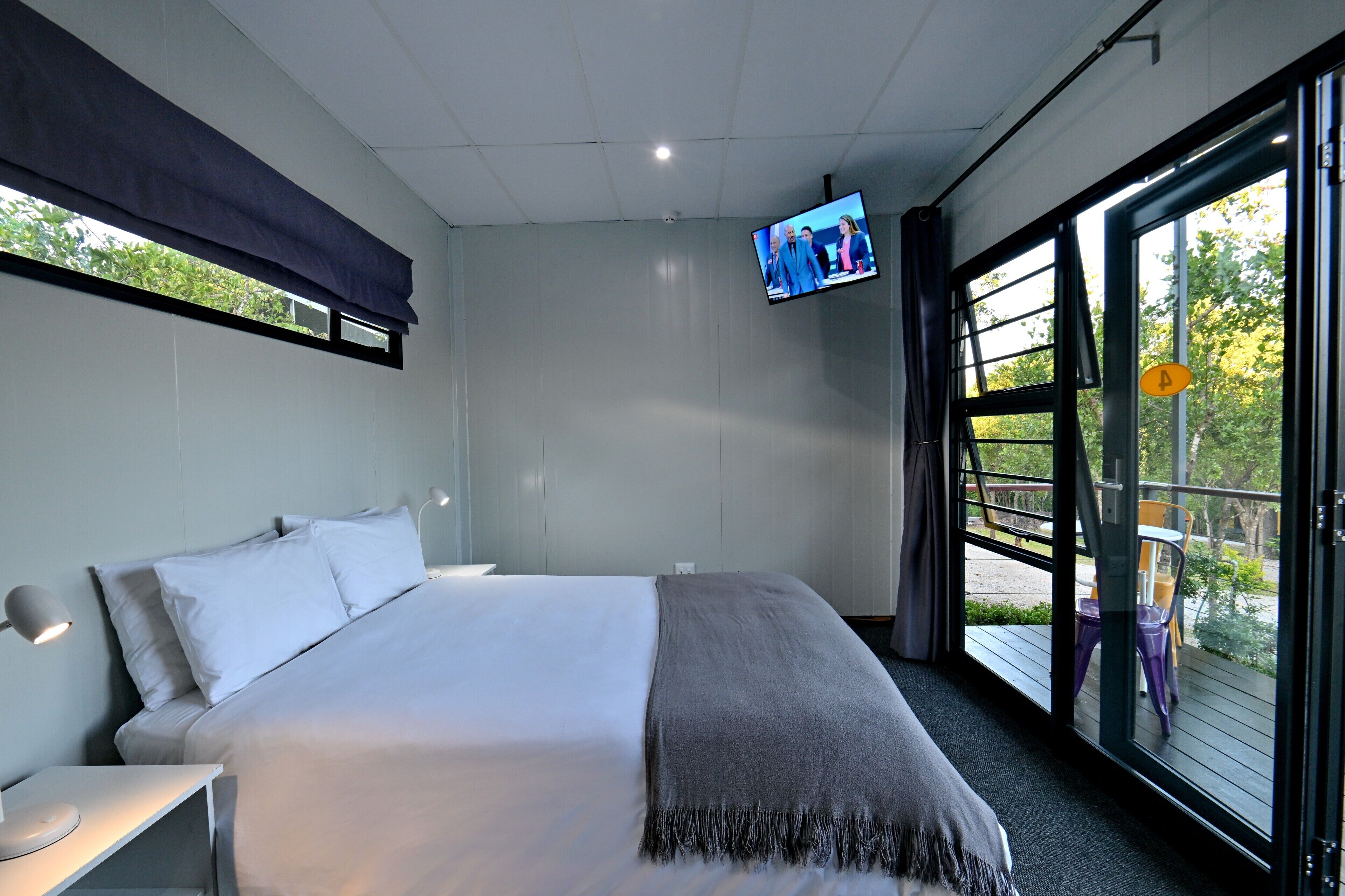 Een moderne hotelkamer met een groot bed, een aan de muur bevestigde televisie en een balkon met buitenmeubilair.