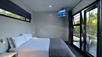 Een moderne hotelkamer met een groot bed, een aan de muur bevestigde televisie en een balkon met buitenmeubilair.