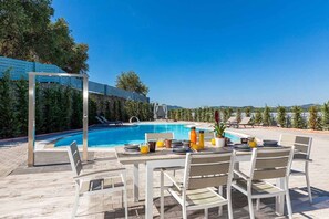 A poolside dining area with a table set for two, surrounded by chairs, and a pool in the background.