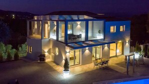 A modern two-story house with a glass facade, outdoor seating area, and a swimming pool. - Five Stars Villa Corfu (Corfu)