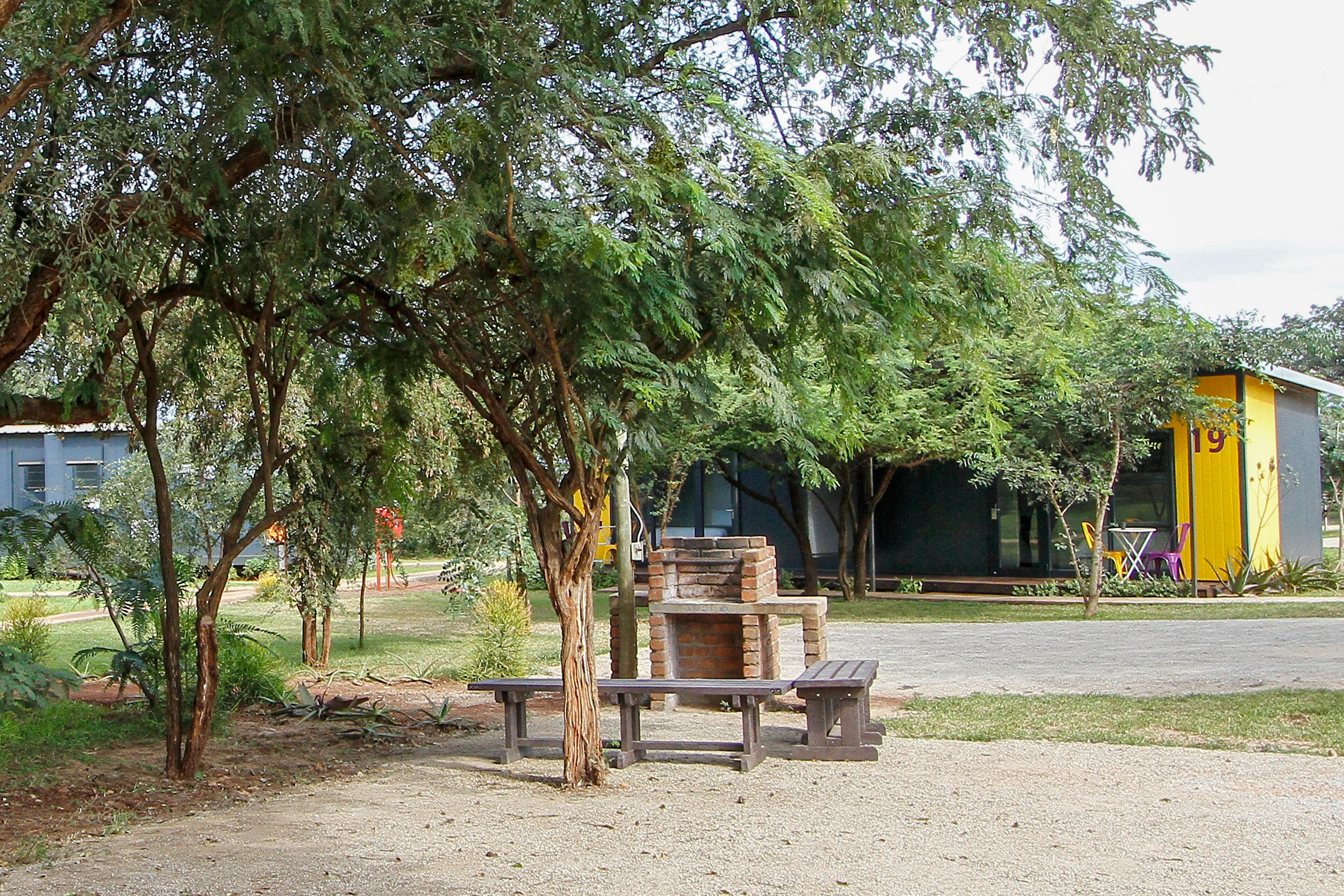 A picnic area with benches, a brick oven, and a yellow building in the background.
