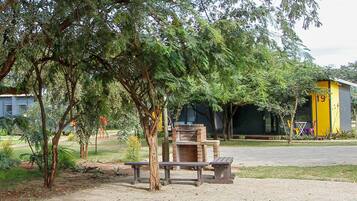 A picnic area with benches, a brick oven, and a yellow building in the background.