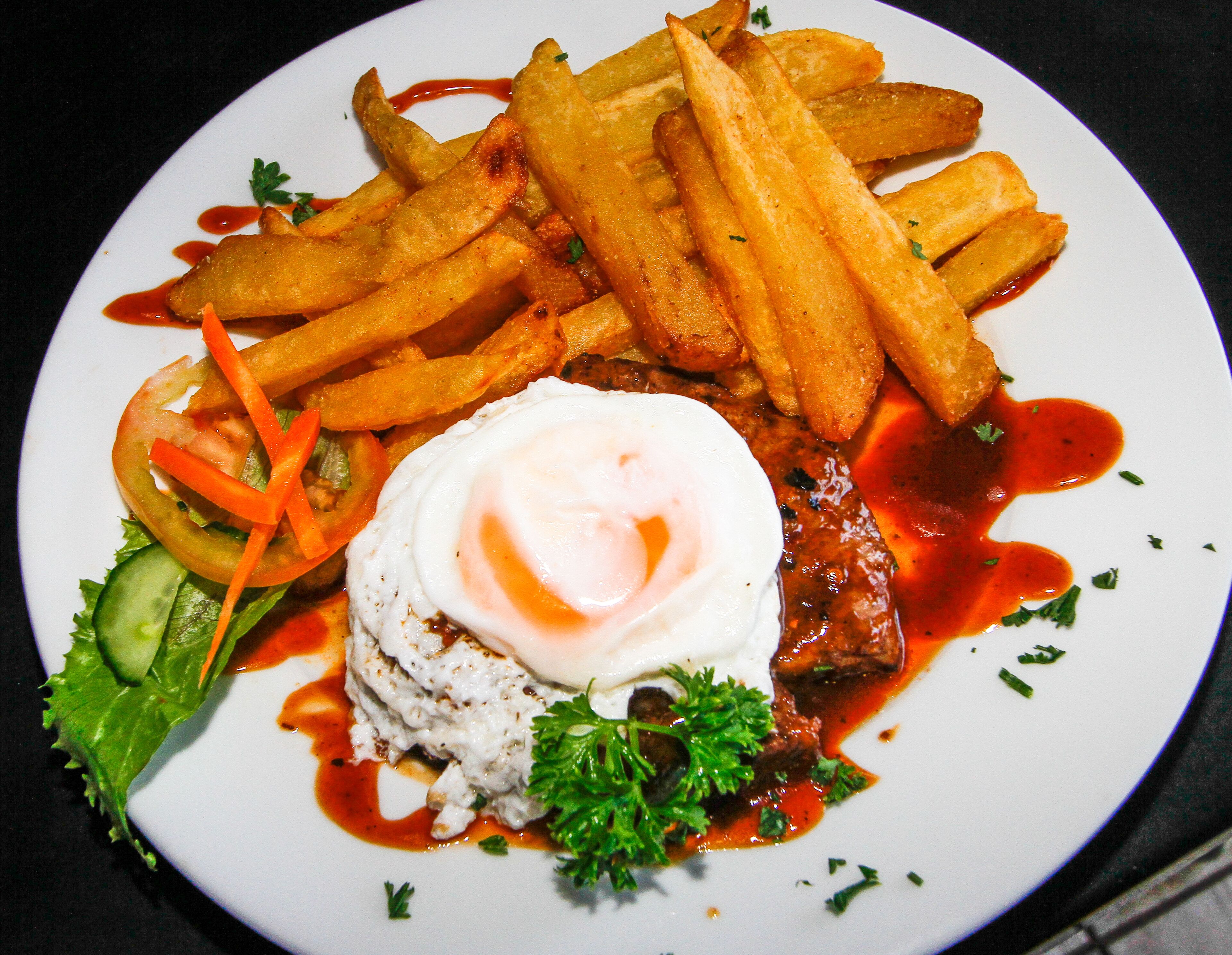 Une assiette de nourriture comprenant des frites, un œuf poché et un plat de viande, le tout garni d’herbes.