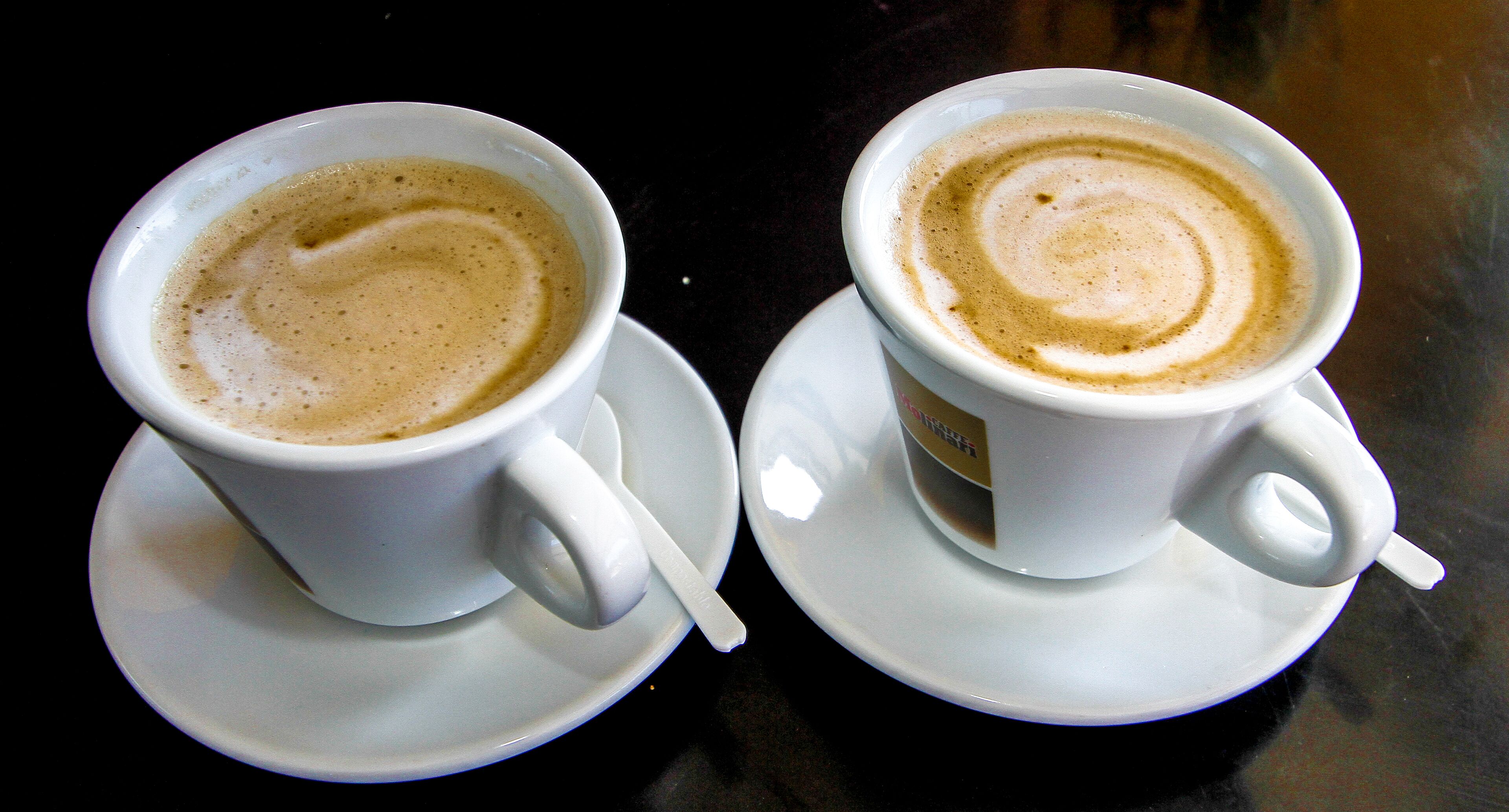 Deux tasses de café blanches, accompagnées de leurs soucoupes, posées sur une surface sombre.