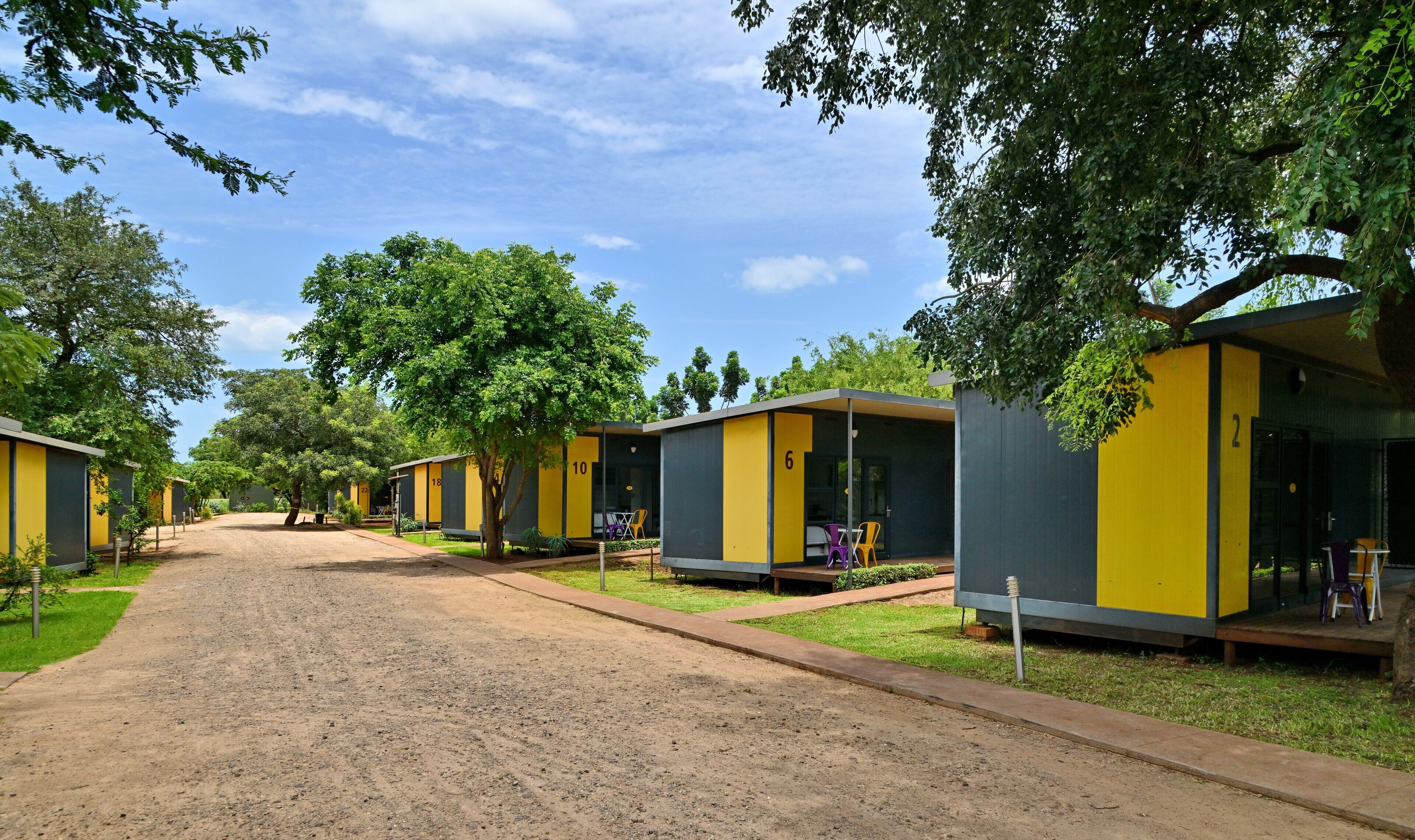 A row of numbered cabins with outdoor seating, surrounded by trees and a gravel path.