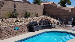 Une piscine dont le bord est revêtu de carreaux, entourée d’une terrasse en béton et d’un mur en briques.