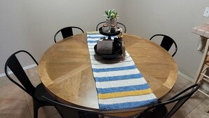 Une table de salle à manger ronde en bois, agrémentée d’un chemin de table rayé bleu et blanc, de chaises noires et d’une petite plante servant de centre de table.