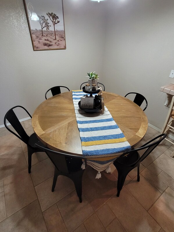 A round wooden dining table with a striped table runner, black chairs, and a small plant centerpiece.