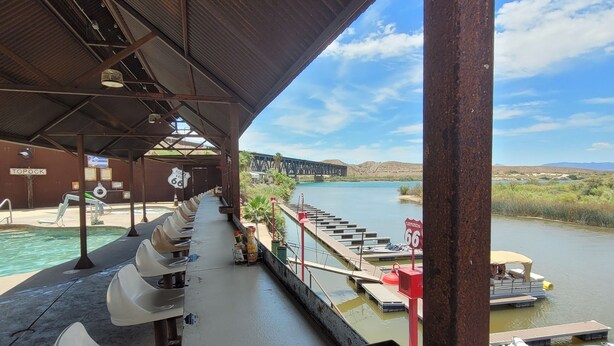 Un espace extérieur abrité, aménagé avec des sièges, et offrant une vue sur une rivière et un pont.