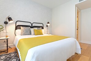 Ein modernes Schlafzimmer mit einem Bett, zwei Nachttischlampen, einem kleinen Tisch mit einer Pflanze und einem gemusterten Teppich.