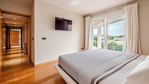 Een slaapkamer met een bed, een aan de muur bevestigde televisie en een groot raam met gordijnen.