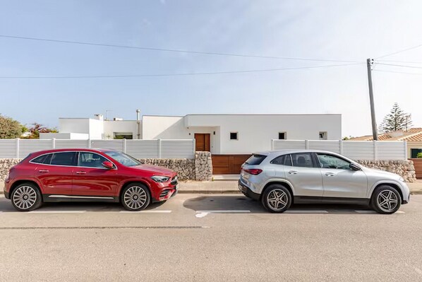 Two cars parked in front of a modern white building with a stone wall and a wooden door.