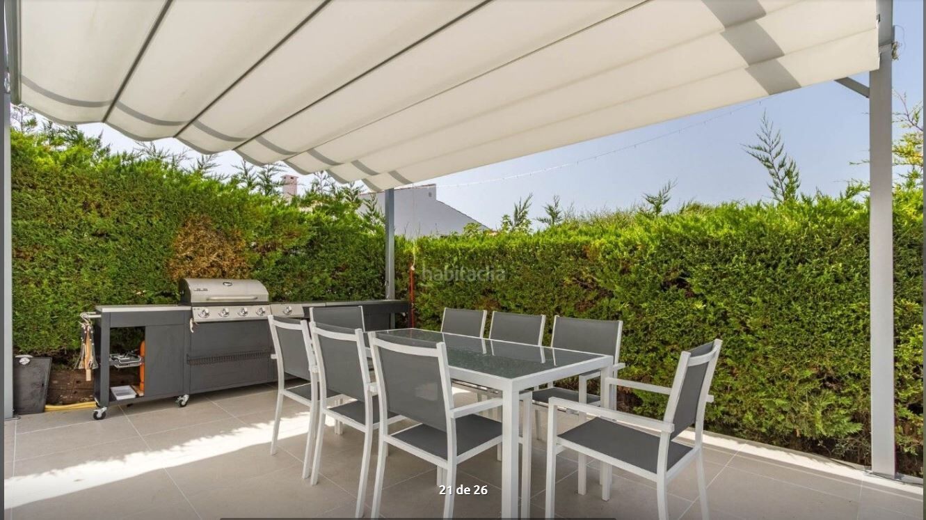 An outdoor patio with a grill and dining table under a white canopy.