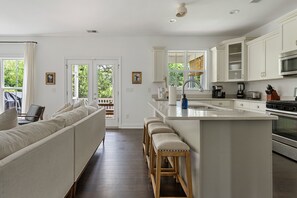 Una cocina moderna con armarios blancos, una isla grande y una zona de estar con sofá y taburetes.