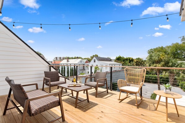 A wooden deck with wicker furniture, a small table, and string lights.