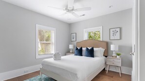 Un dormitorio con cama, mesitas de noche, ventilador de techo y ventanas.