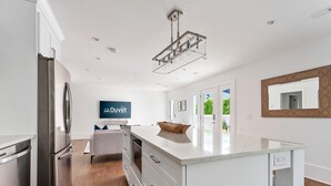 Una cocina moderna con un refrigerador de acero inoxidable, una isla grande con encimera de mármol y una lámpara colgante.