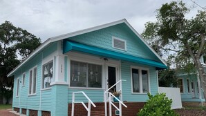 A single-story house with a blue exterior, white trim, and a brick foundation. It features a front porch with a white railing and a small set of steps leading to the entrance. - 2-Bedroom house with a great yard in down town (New Smyrna Beach)