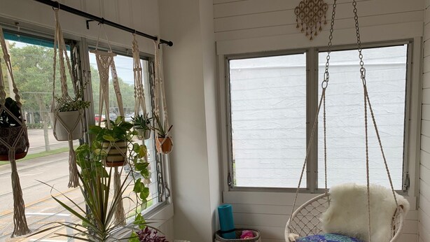 A room with a macrame hanging plant, a macrame chair, and a view of a body of water through a large window. - 2-Bedroom house with a great yard in down town (New Smyrna Beach)