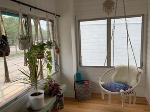 Une pièce décorée d’une plante suspendue en macramé, d’une chaise en macramé et offrant une vue sur un plan d’eau grâce à une grande fenêtre.