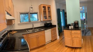 A modern kitchen with wooden cabinets, a black countertop, a dishwasher, and a coffee machine. - 2-Bedroom house with a great yard in down town (New Smyrna Beach)
