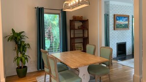 A dining area with a wooden table and four chairs, a hanging light fixture, a bookshelf, a potted plant, and a view of a brick wall and fireplace. - 2-Bedroom house with a great yard in down town (New Smyrna Beach)
