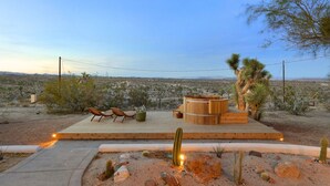 An outdoor deck with seating and a wooden structure, surrounded by desert vegetation and a distant landscape.