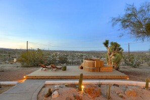An outdoor deck with seating and a wooden structure, surrounded by desert vegetation and a distant landscape.