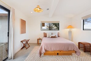 A bedroom with a bed, a bedside table, a lamp, and a view of the outdoors. - TerraCasa-Hot Tub, Fire Pit,Outdoor Shower &Views! (Yucca Valley)