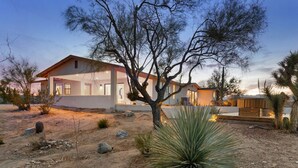 A modern house with a large patio area, surrounded by desert vegetation.