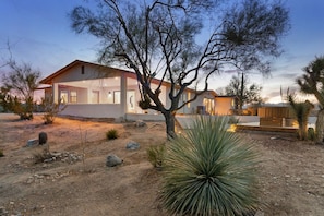 A modern house with a large patio area, surrounded by desert vegetation.
