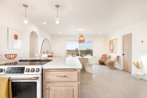 A modern kitchen with a large island, a dining area with chairs, and a view of the desert through a window.